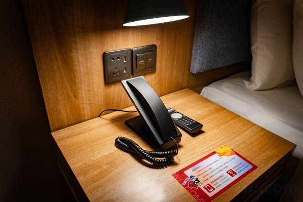 Una habitación de hotel con teléfono en la mesita de noche, una lámpara y una cama.
