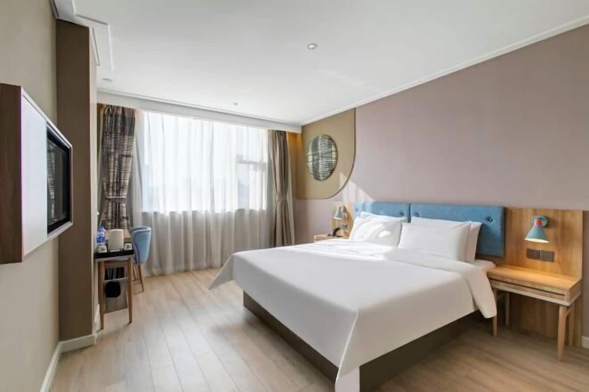 Une chambre d’hôtel avec un grand lit, un bureau avec une chaise, une télévision et une fenêtre avec des rideaux.