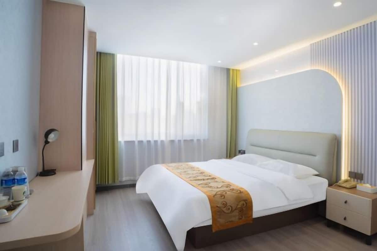 Une chambre d’hôtel avec un lit, une table de chevet, une lampe et une fenêtre avec des rideaux.