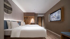 Hotellihuone, jossa on suuri sänky, työpöytä, televisio ja seinälle asennettu näyttö.