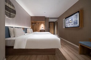 Ein Hotelzimmer mit einem großen Bett, einem Schreibtisch, einem Fernseher und einem wandmontierten Bildschirm.
