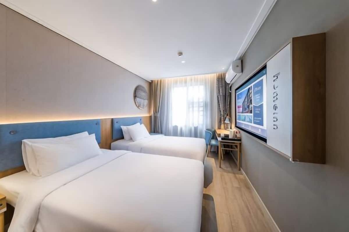 Une chambre d’hôtel avec deux lits, un bureau, une chaise et un grand écran affichant des informations.
