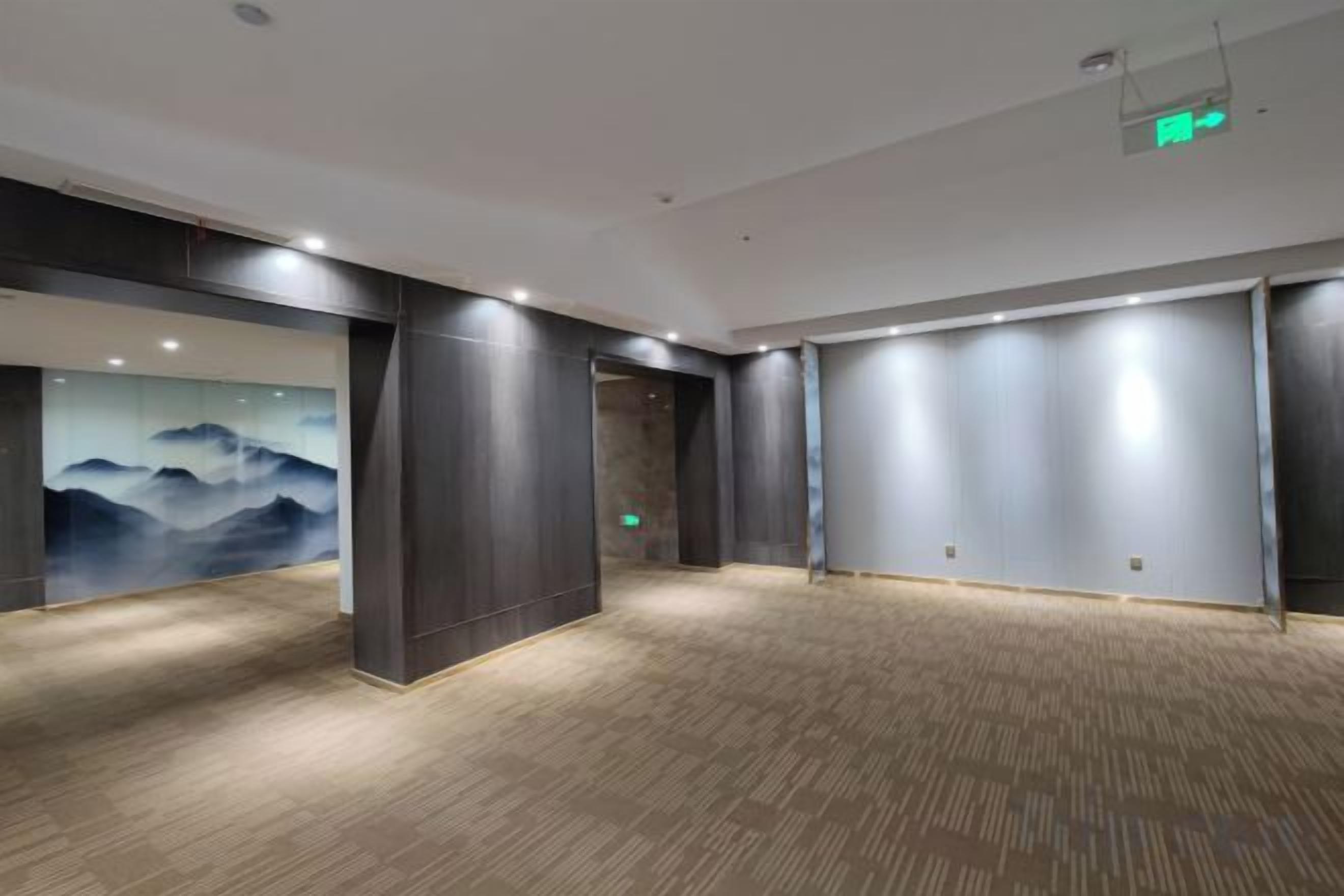 A hotel lobby with a large wall mural, a carpeted floor, and a modern ceiling design.