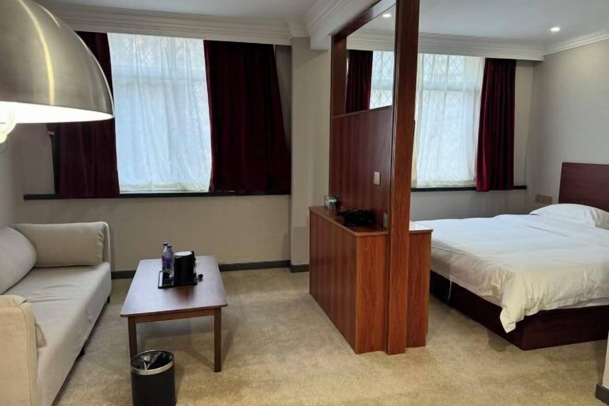 A hotel room with a bed, a sofa, a table, a desk, and a window with curtains.