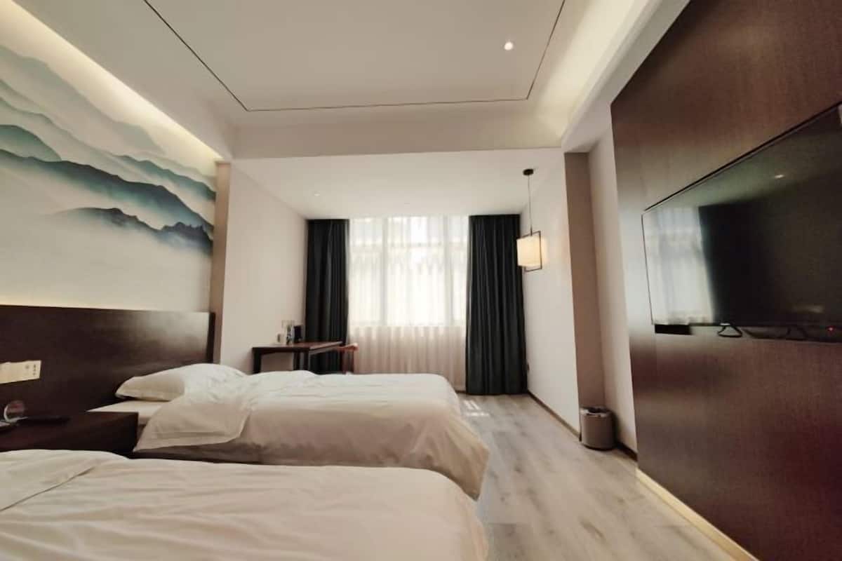 A hotel room with two beds, a TV, a painting on the wall, and a view of the room.