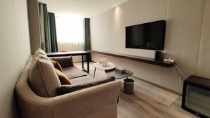 A modern living room with a sofa, a coffee table, a TV mounted on the wall, and a small table with a remote control. - Zhengzhou Yindu Hotel (China Great Wall Aluminum) (Zhengzhou)