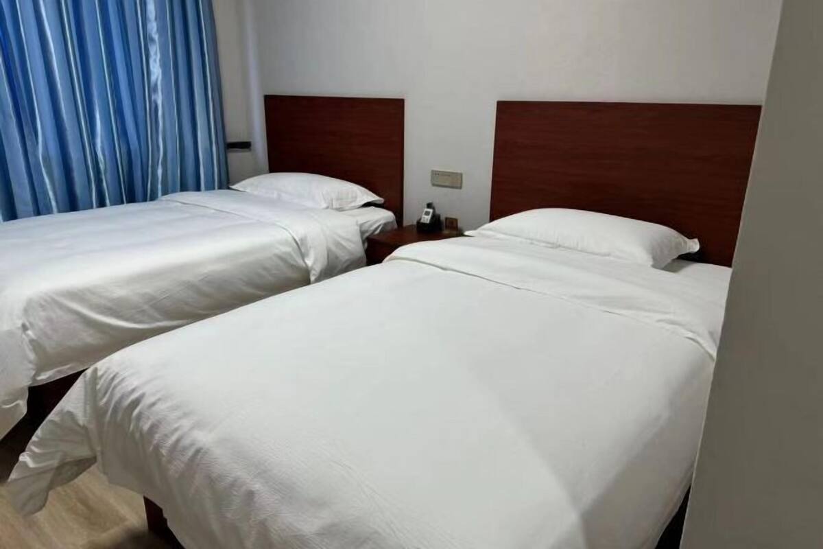 Two single beds with wooden headboards, a bedside table with a phone, and a blue curtain.