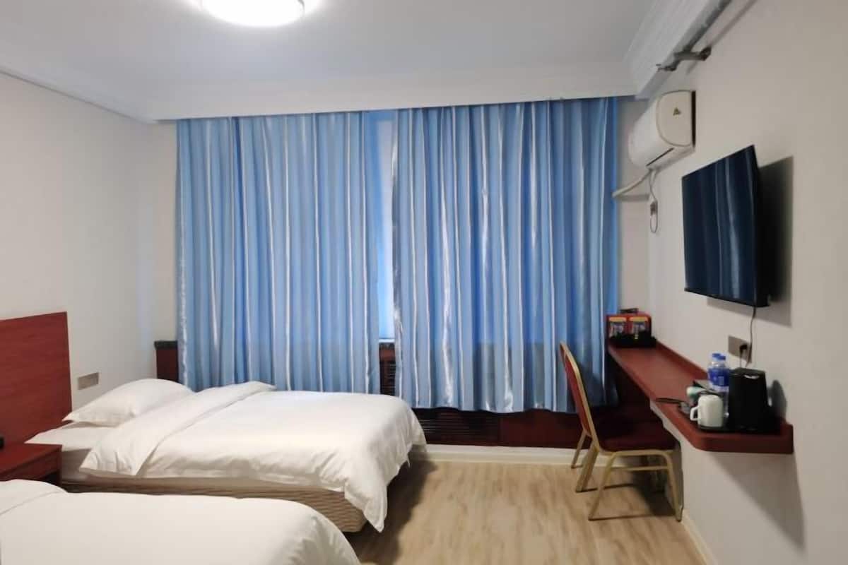 A hotel room with two beds, a TV, a desk with a chair, and a window with curtains.