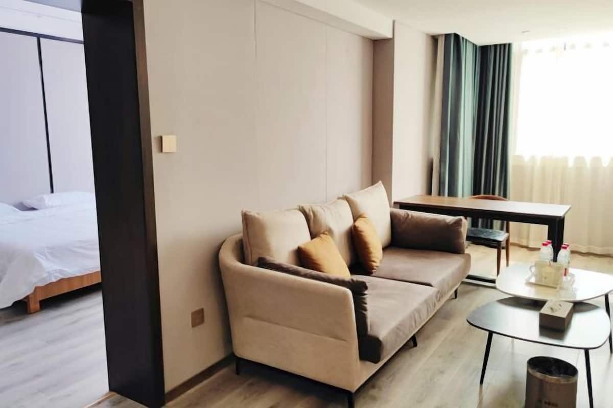 A modern hotel room with a sofa, a small table, a bed, and a window with curtains.
