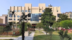 A modern building with a central glass facade, surrounded by a well-maintained garden with various trees and a paved walkway. - Zhengzhou Yindu Hotel (China Great Wall Aluminum) (Zhengzhou)