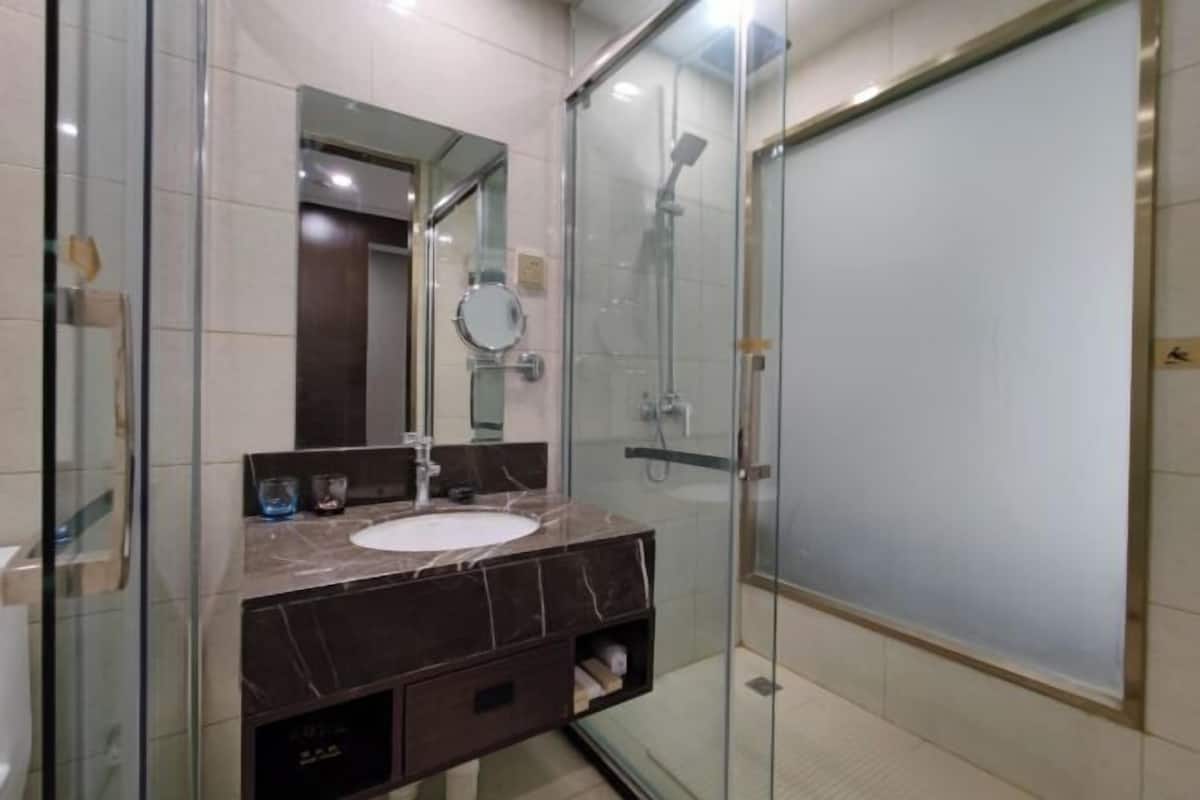 A modern bathroom with a glass-enclosed shower, a marble sink, and a mirror.