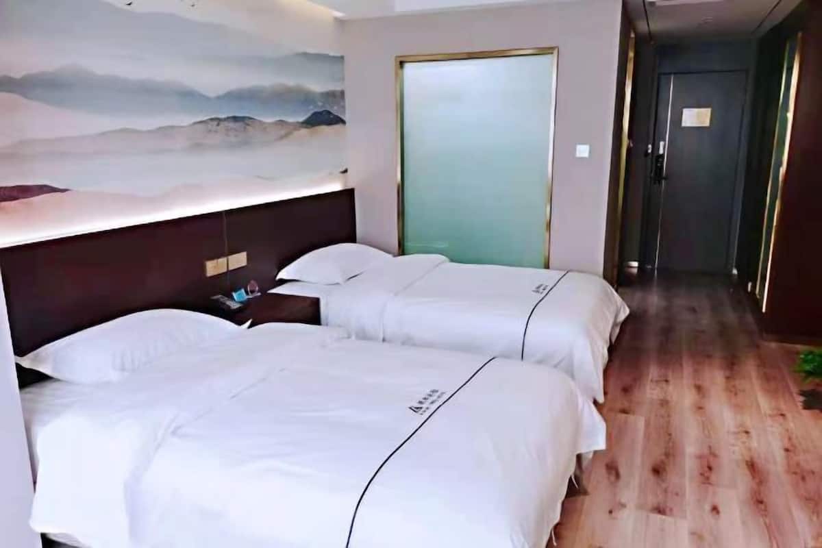A hotel room with two beds, a nightstand, a wall-mounted lamp, and a door with frosted glass.