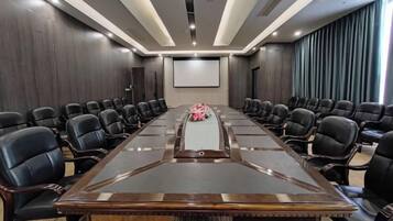 A conference room with a long table and multiple chairs, a projector screen, and a large window with curtains.