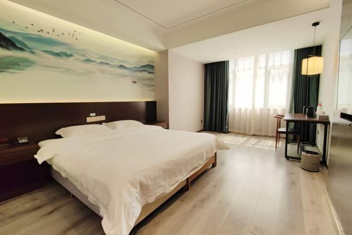 A hotel room with a large bed, a desk, a chair, a lamp, and a painting on the wall.