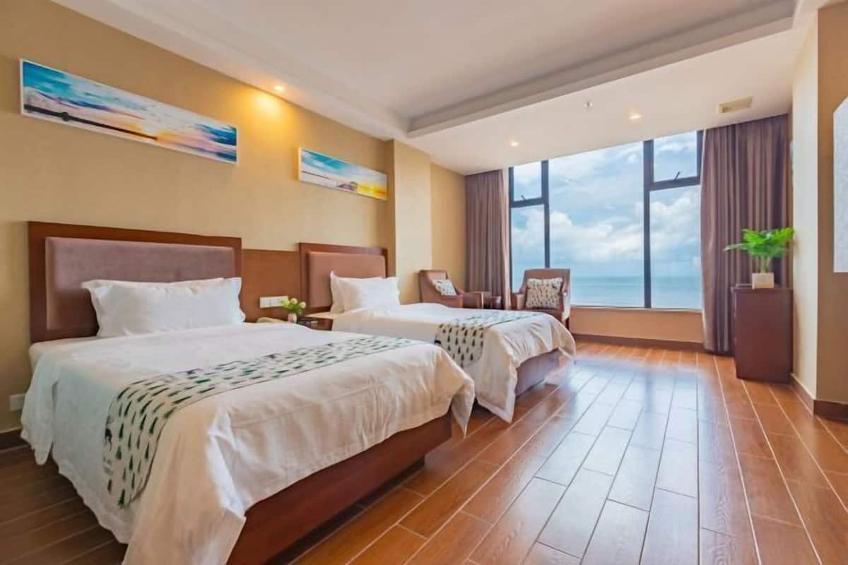 A hotel room with two beds, a large window with a view, and a plant on the windowsill.