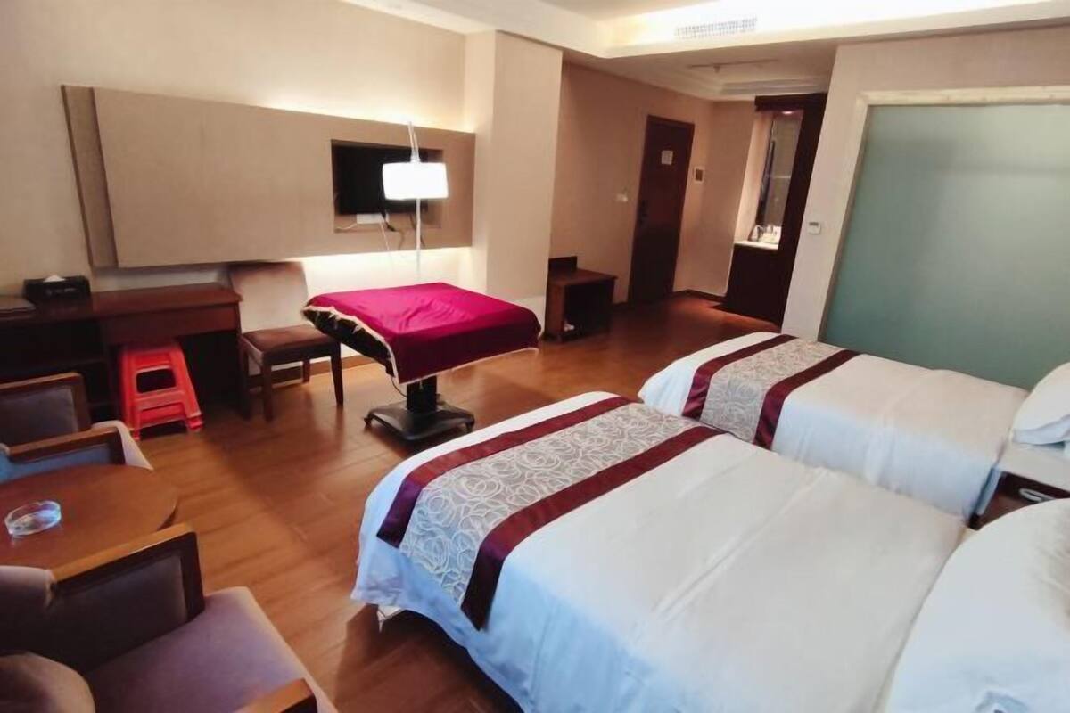 A hotel room with two beds, a desk, a chair, a small stool, and a television.