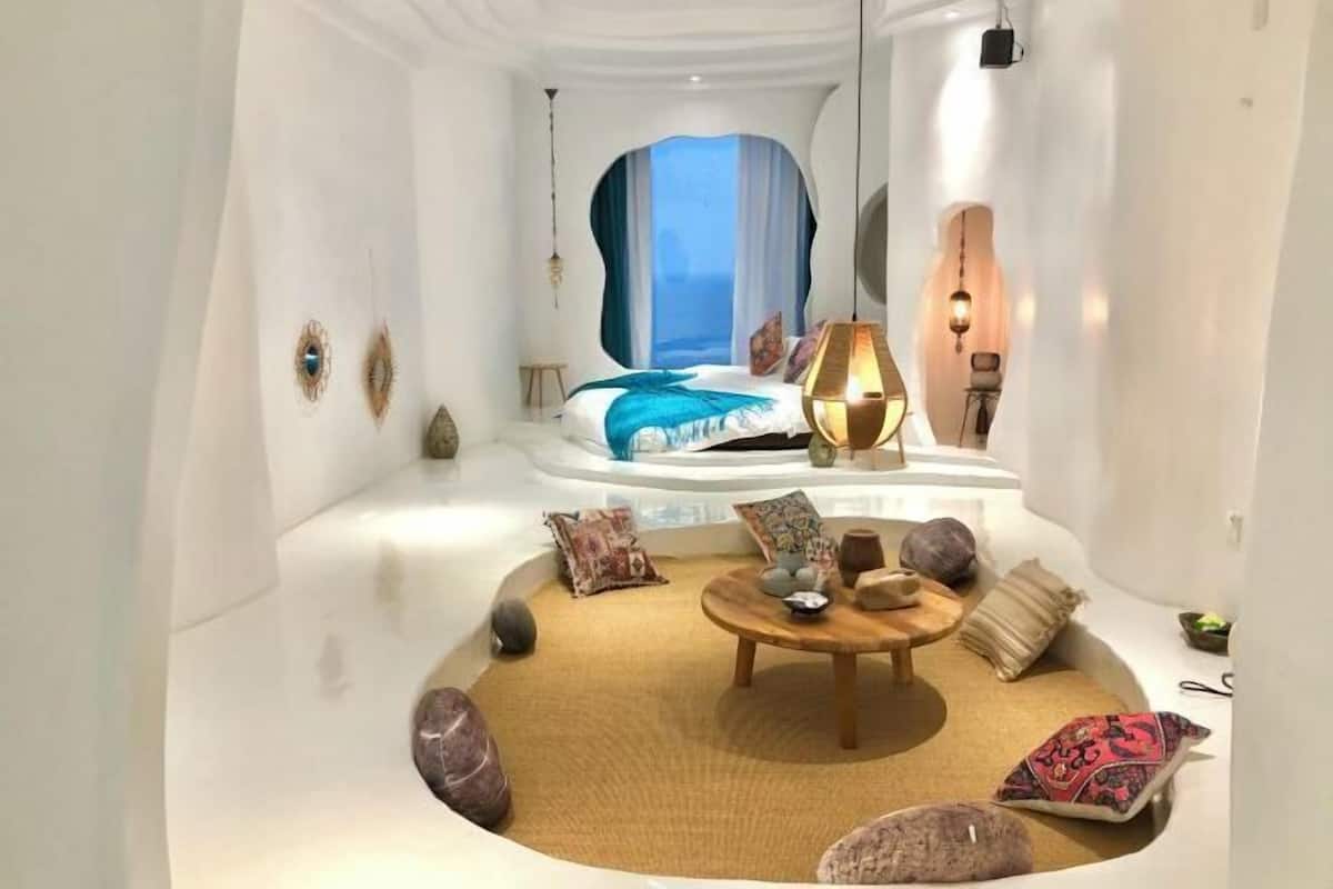 A modern room with a curved ceiling, a bed with a view, a round wooden table, and decorative pillows.