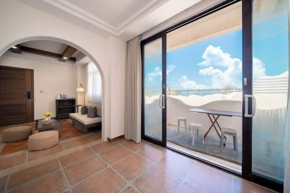 A spacious living area with a sliding glass door leading to a balcony with a view of the beach.