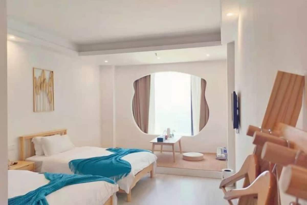 A hotel room with two beds, a round mirror, a small table, and a chair.