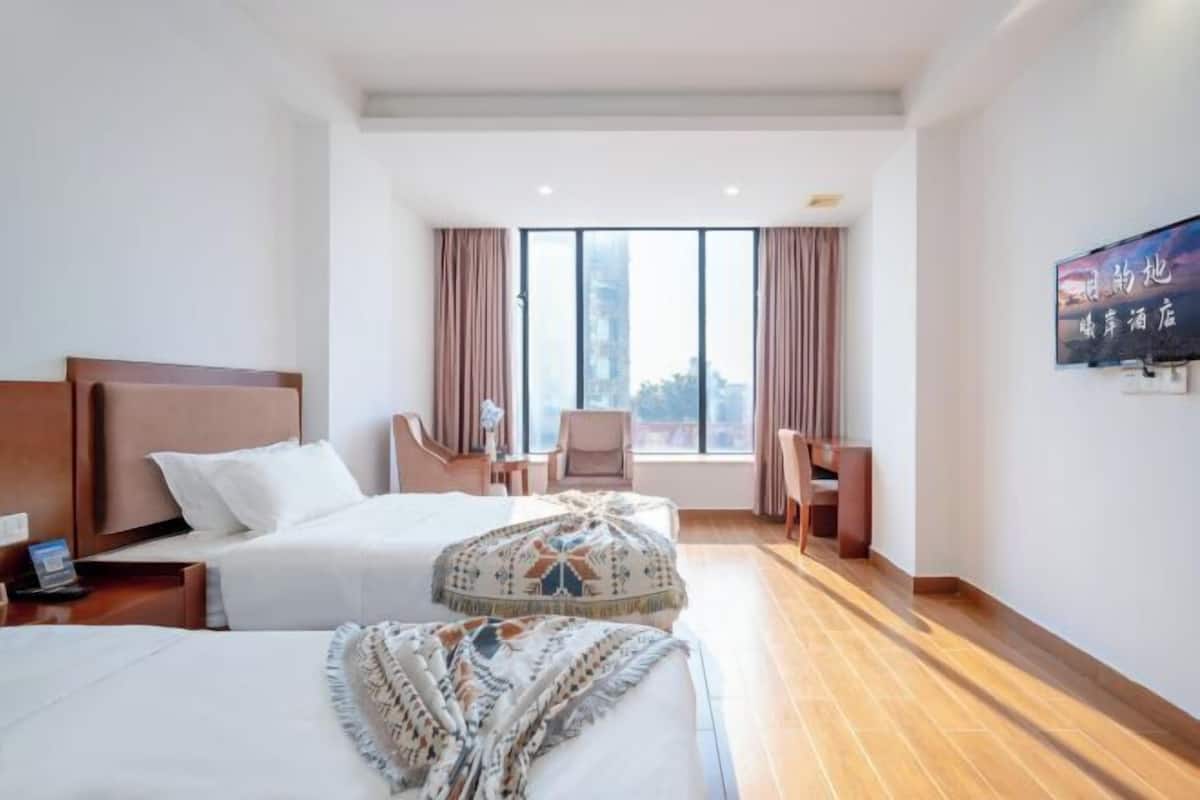 A hotel room with two beds, a desk, a chair, and a large window with curtains.