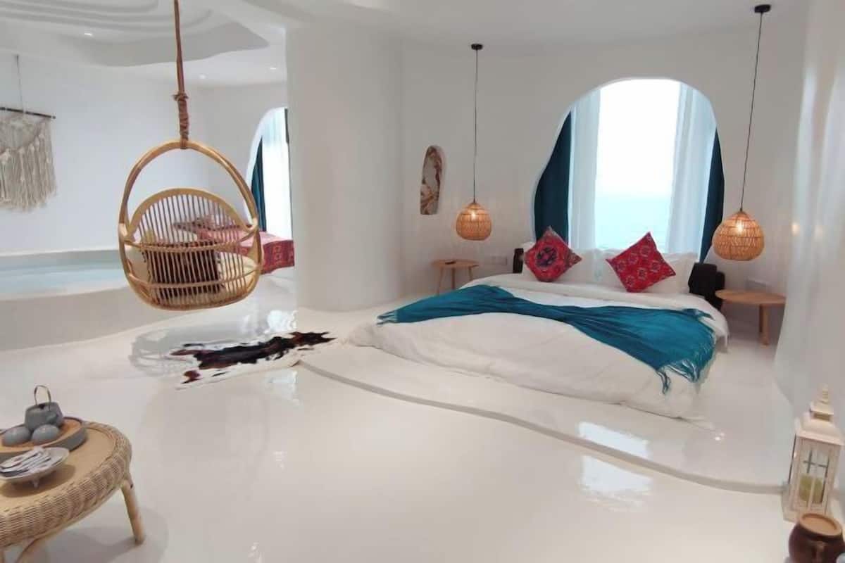 A modern bedroom with a large bed, hanging chair, and decorative lighting.