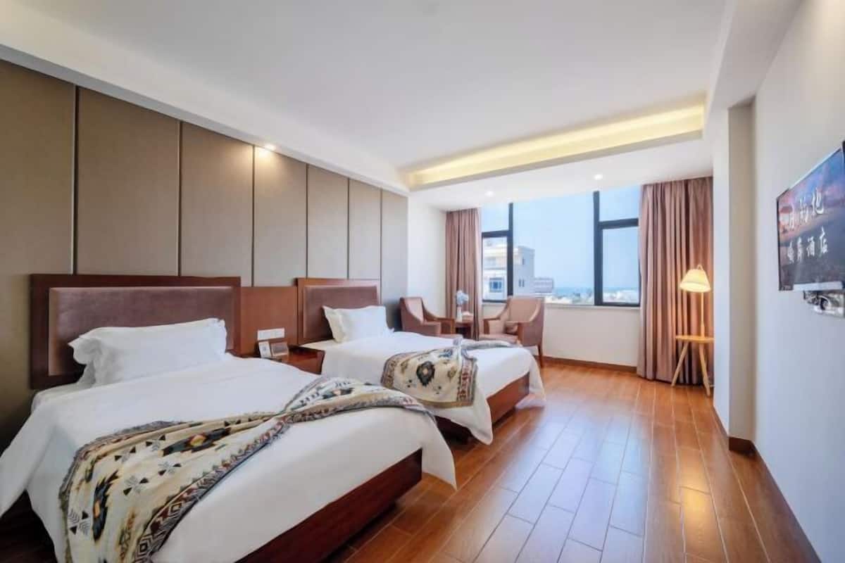 A hotel room with two beds, a view of the city, and a large window.