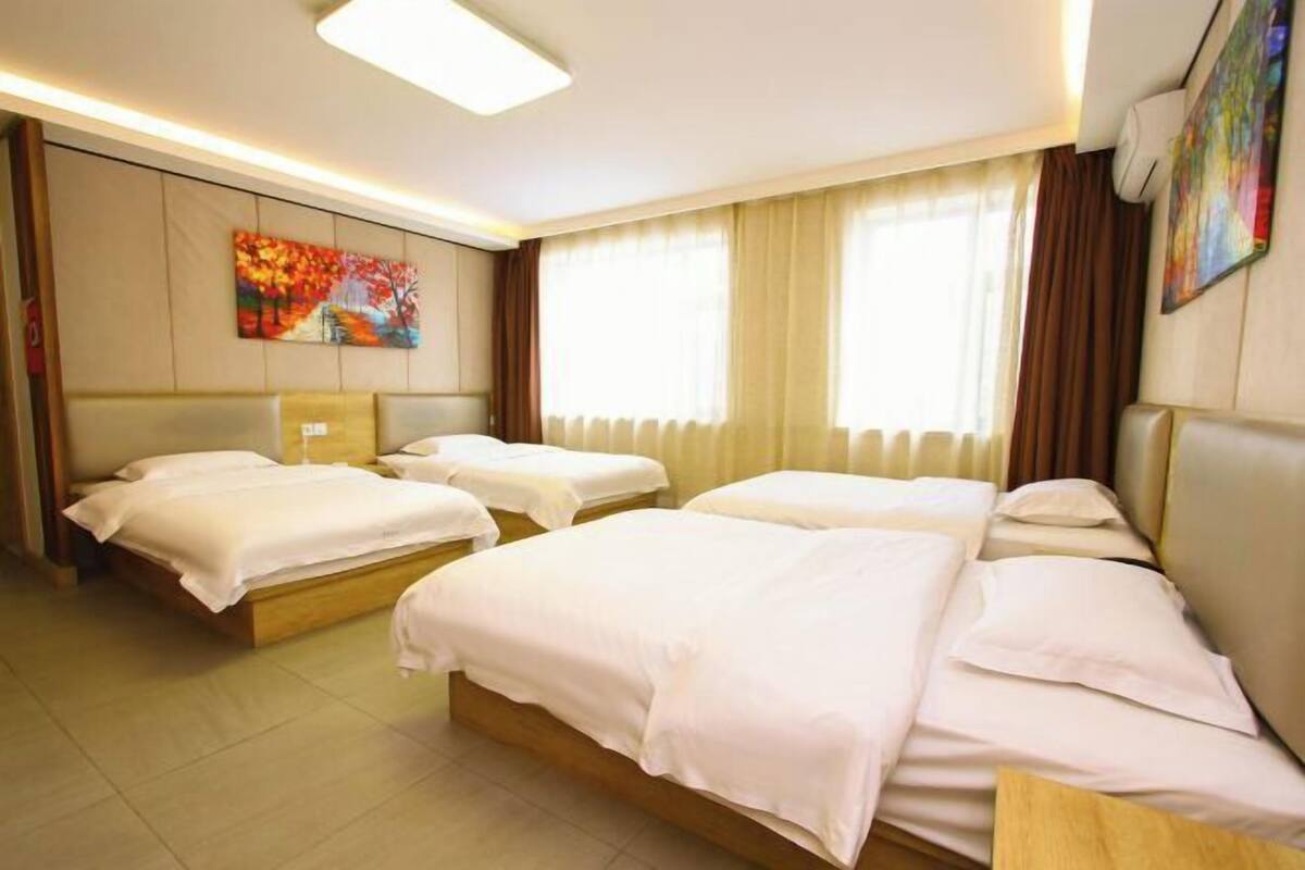 Habitación de hotel con tres camas, un ventanal con cortinas y un cuadro en la pared.