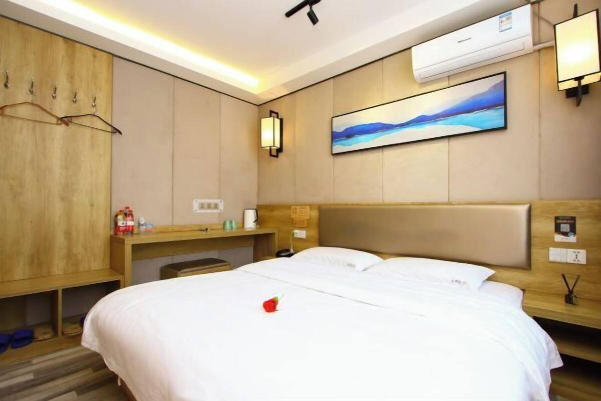 Una habitación de hotel con una cama, un armario de madera, un escritorio con una lámpara y un cuadro en la pared.