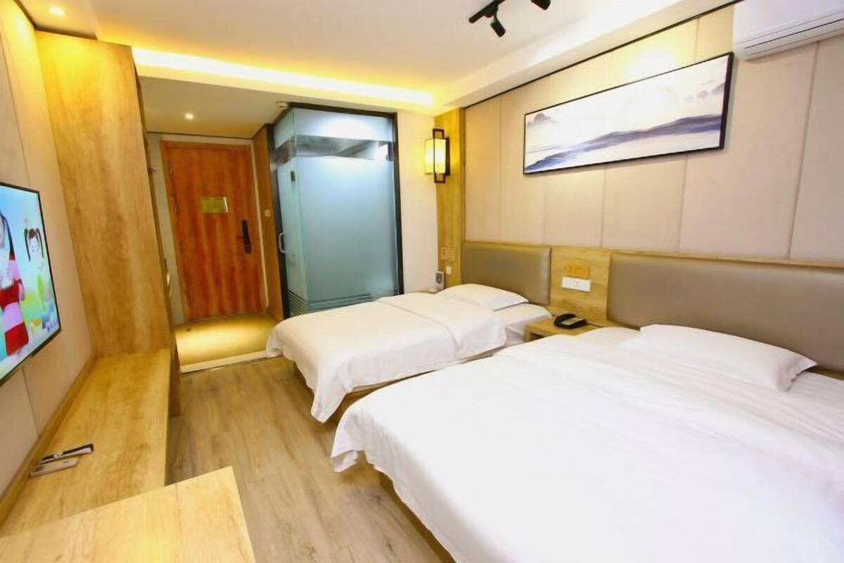 Habitación de hotel con dos camas, televisión, escritorio de madera y puerta que da a un pasillo.