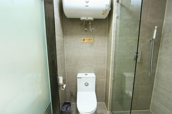A small, compact bathroom with a toilet, a glass-enclosed shower, and a toilet paper holder. - Jinhui Fashion Hotel (Baicheng)