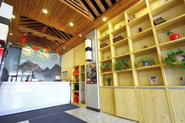 A reception area with a wooden reception desk, shelves with plants, and a wall mural. - Jinhui Fashion Hotel (Baicheng)