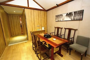 A dining area with a wooden table and chairs, a small side table with a kettle, and a framed picture on the wall. - Jinhui Fashion Hotel (Baicheng)