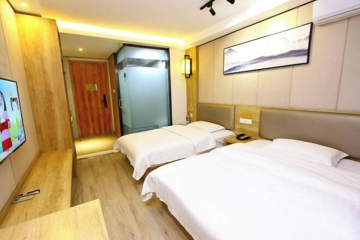 Habitación de hotel con dos camas, televisión, piso de madera, una puerta y una lámpara fijada a la pared.