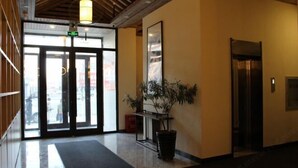 Een hotellobby met een receptiebalie, een potplant en een lift.