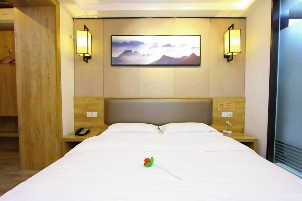 Una habitación de hotel con una cama, dos lámparas de noche, un cuadro en la pared y un cabecero de madera.