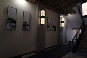 A hallway with framed artwork on the walls, a staircase, and wall-mounted lighting fixtures. - Jinhui Fashion Hotel (Baicheng)