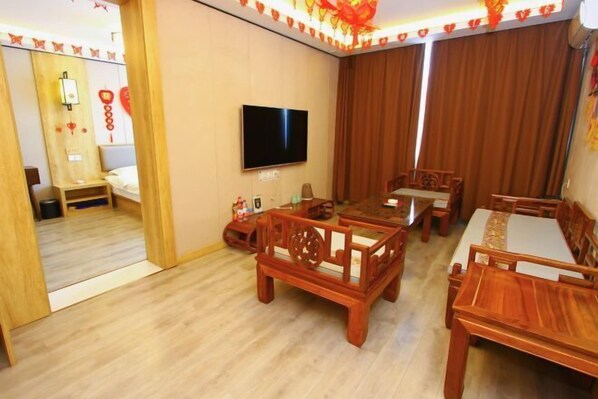 A hotel room with a wooden floor, a TV mounted on the wall, a bed, and a dining area with wooden furniture. - Jinhui Fashion Hotel (Baicheng)