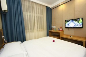 A hotel room with a bed, a TV on the wall, a desk with a lamp, and a window with curtains. - Jinhui Fashion Hotel (Baicheng)