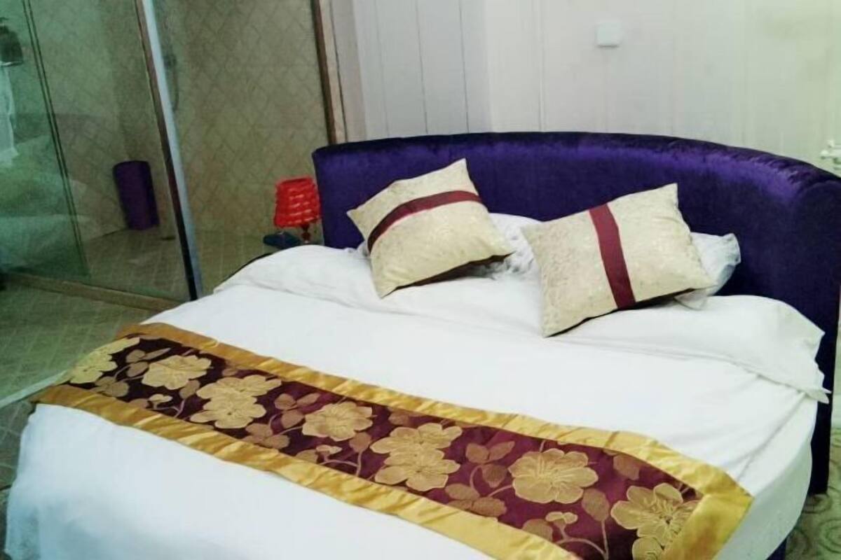 A bed with a purple headboard, white bedding, and a floral-patterned bedspread.