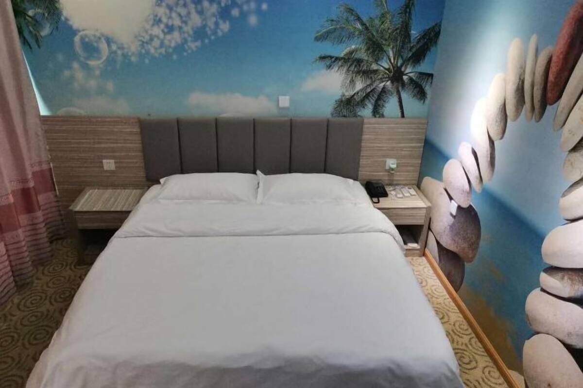 A hotel room with a bed, nightstand, and a mural of a beach scene.