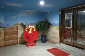 Un'area reception con un elemento decorativo rosso, una pianta in vaso e una porta con pannelli di vetro.