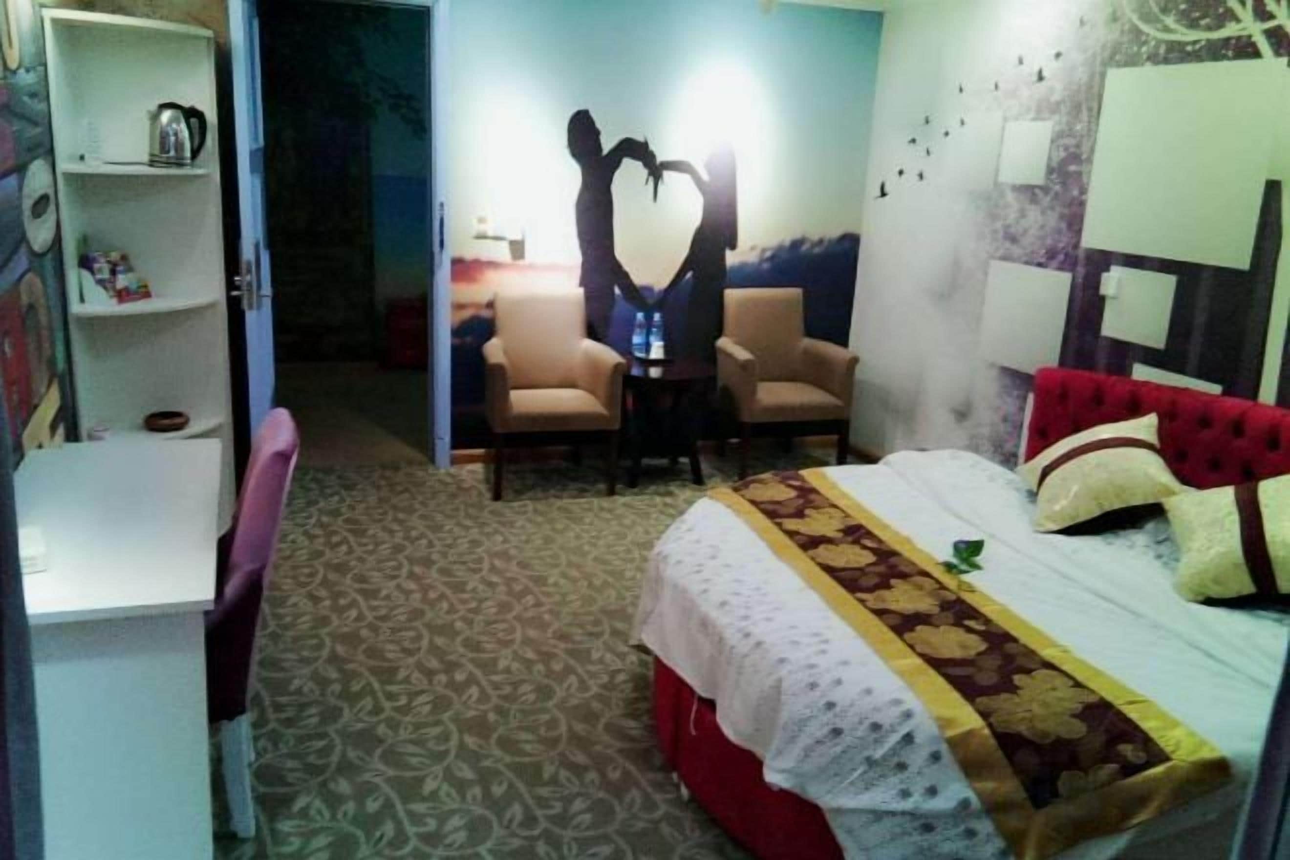 Quarto de hotel com uma cama, duas cadeiras, uma escrivaninha e uma estante.