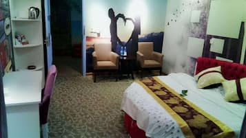 Quarto de hotel com uma cama, duas cadeiras, uma escrivaninha e uma estante.