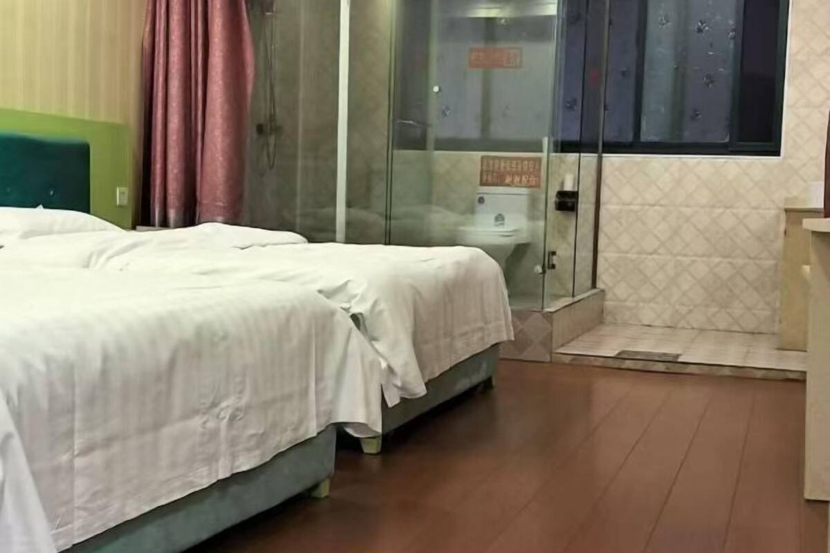 A hotel room with a bed, a glass shower enclosure, and a window with a view.