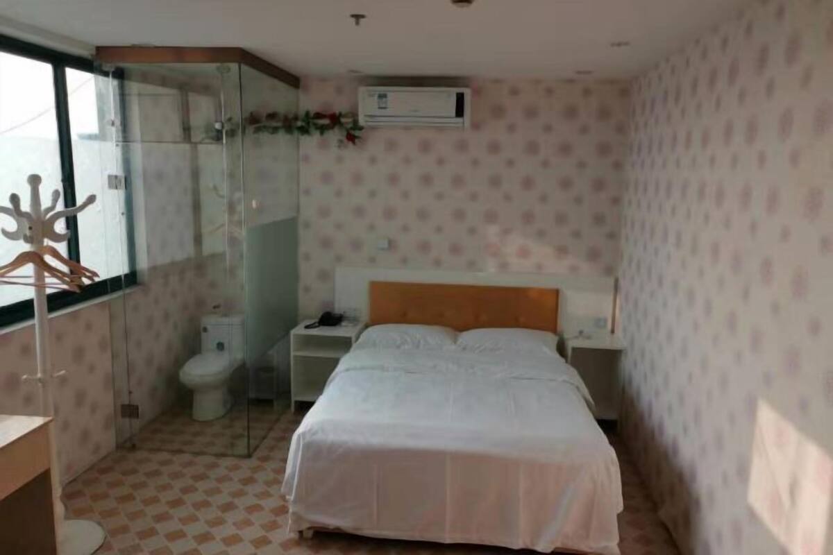 A bedroom with a bed, a bedside table, a nightstand, a toilet, and a glass-enclosed shower.