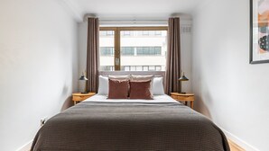 A bedroom with a large bed, two bedside tables, a window with curtains, and a framed picture on the wall.