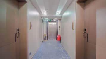 A hotel corridor with a blue carpet, wooden doors, and a visible elevator.