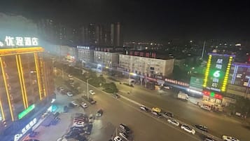 A multi-story building with illuminated signage, a parking lot with several cars, and a busy street with traffic.