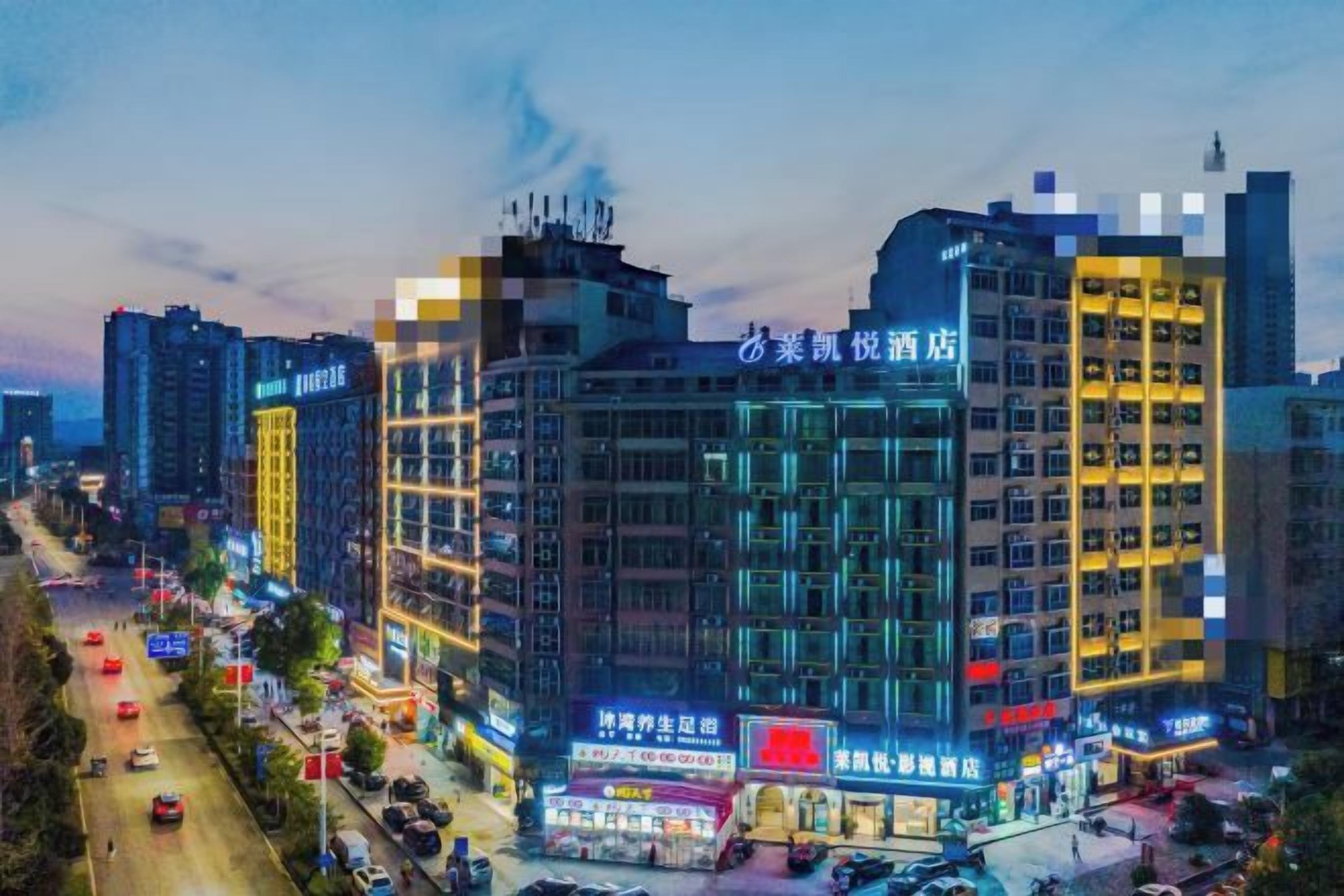 Un hotel de varios pisos con señalización iluminada, una calle concurrida en primer plano y otros edificios al fondo.