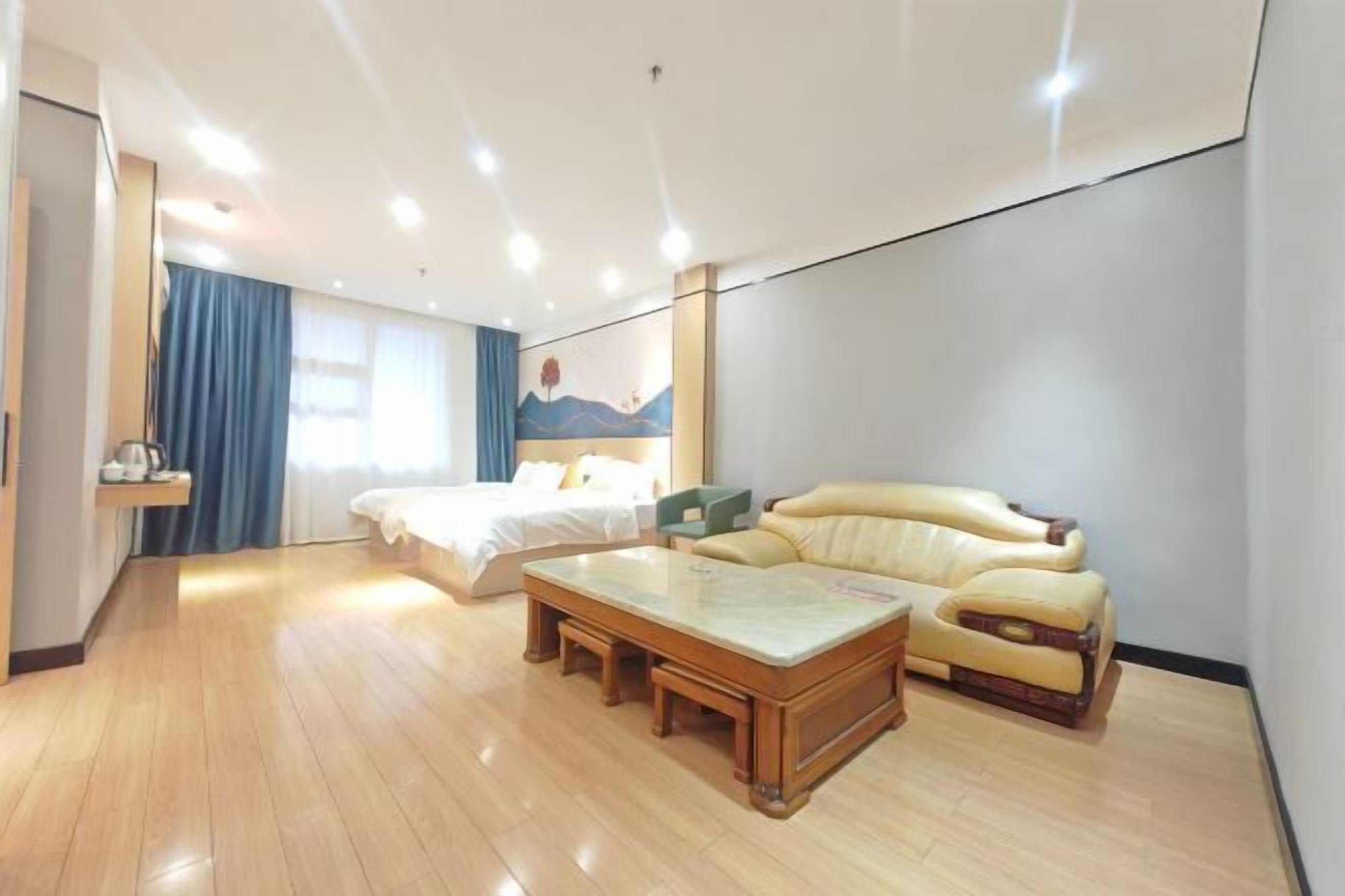 A hotel room with a wooden floor, a bed, a sofa, a coffee table, and a wall with a painting.